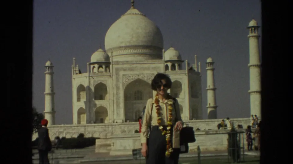 Close visitor-shot 1974 frame of a garlanded woman posing in sunglasses with the Taj Mahal facade and minarets behind her.