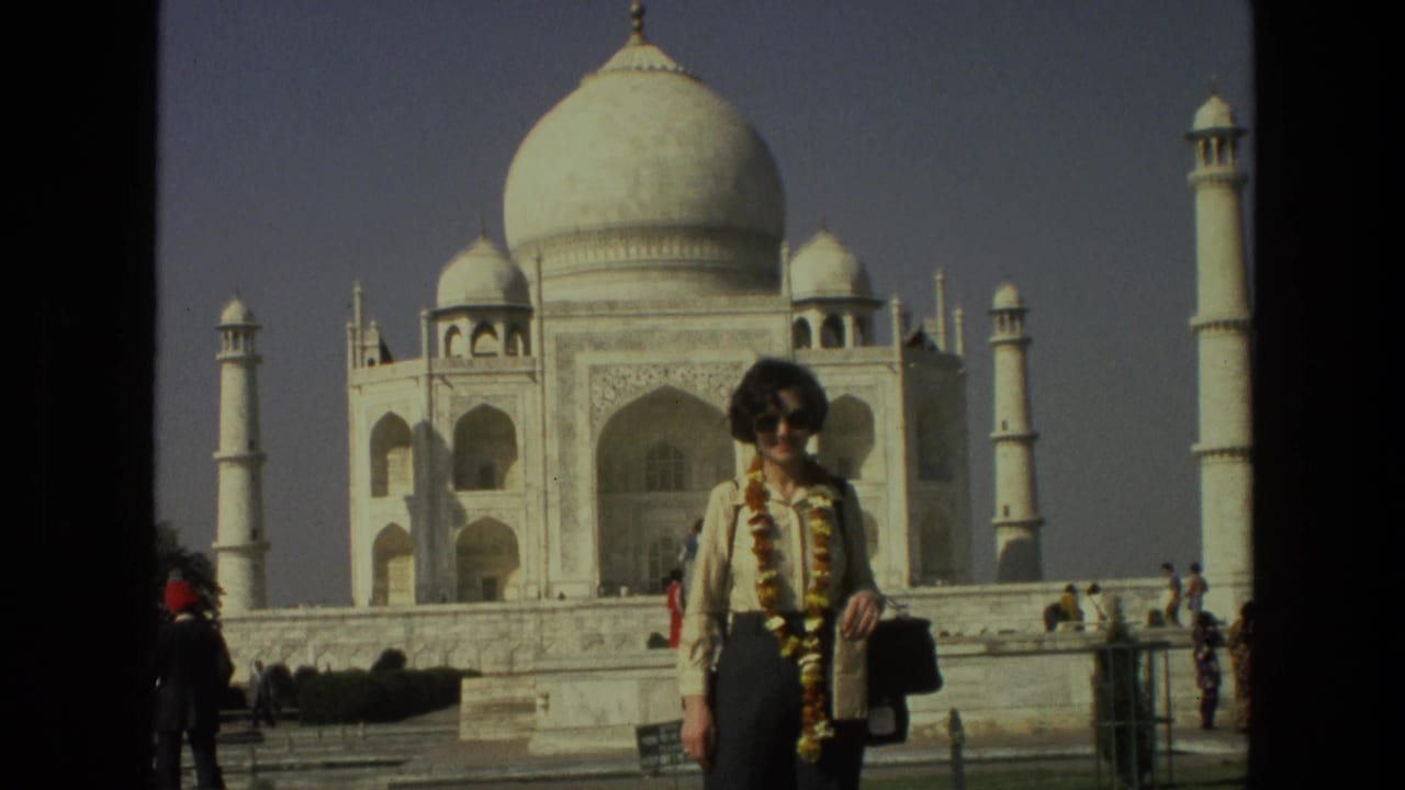 Woman wearing sunglasses and a floral garland stands before the Taj Mahal.