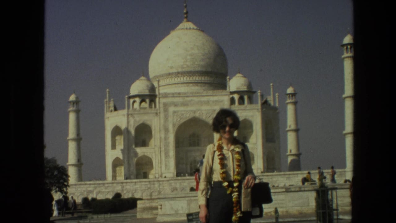 Woman with floral garland poses in front of the Taj Mahal and minarets.