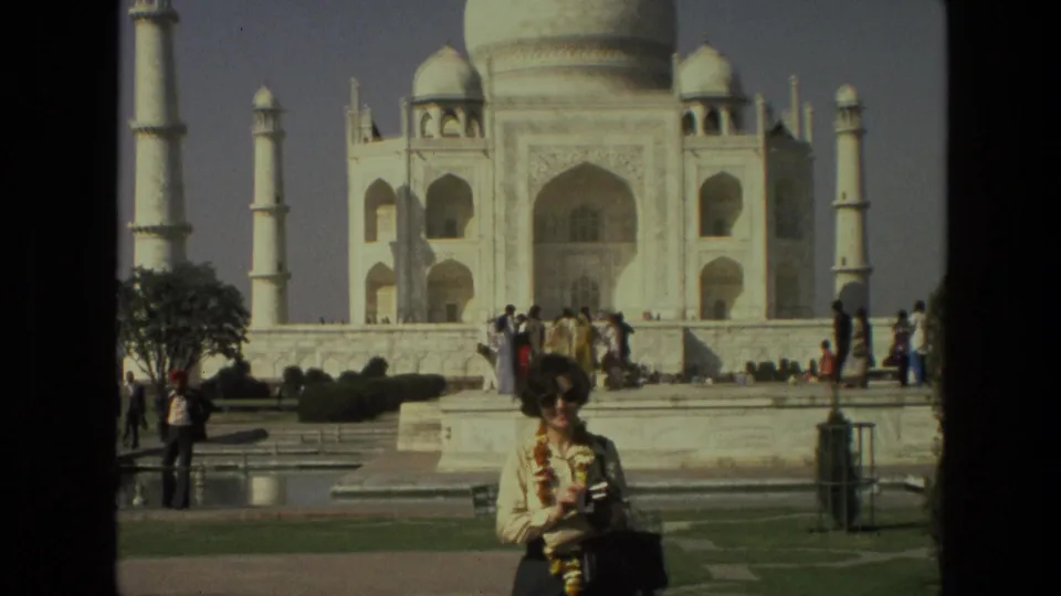 Wider 1974 India home-movie view of the Taj Mahal grounds with a garlanded woman posing in the foreground.