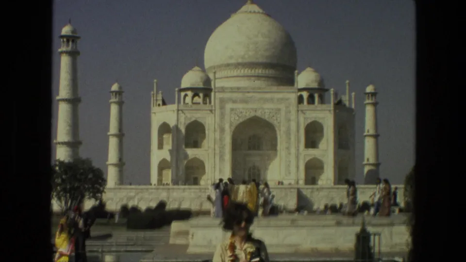 1974 India travel footage frame showing the Taj Mahal, tourists near the platform, and a cropped foreground visitor.