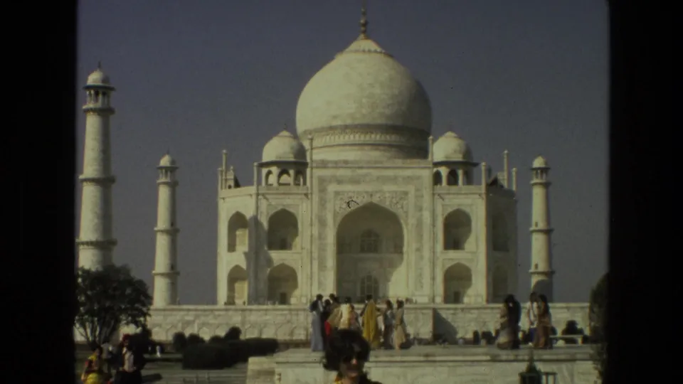 1974 8mm frame of the Taj Mahal facade and minarets, with tourists standing and walking along the platform below.