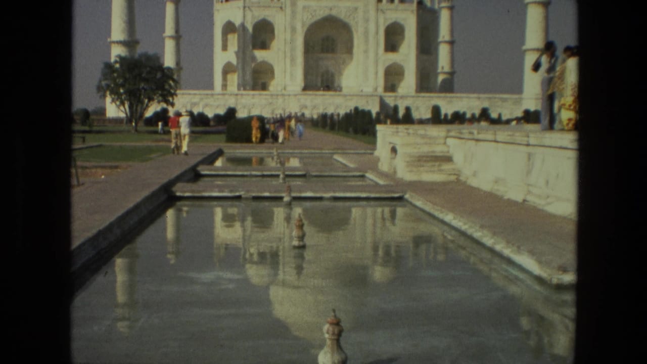 Taj Mahal seen across a reflecting pool with tourists walking in the gardens.