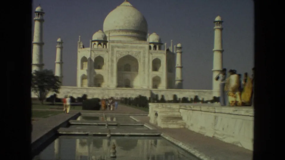 1974 8mm frame looking toward the Taj Mahal dome and minarets, with tourists moving beside the reflecting pool in the foreground.