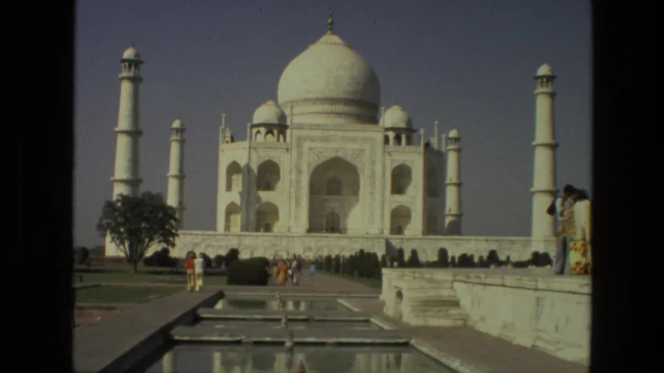 1974 home-movie frame of tourists in the Taj Mahal gardens, with the reflecting pool leading toward the white marble mausoleum.