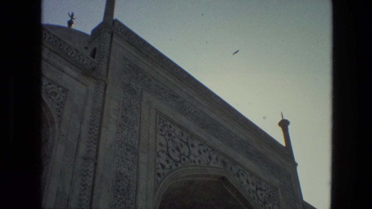 Low-angle view of a carved mosque facade with an arch and a small bird in the sky.