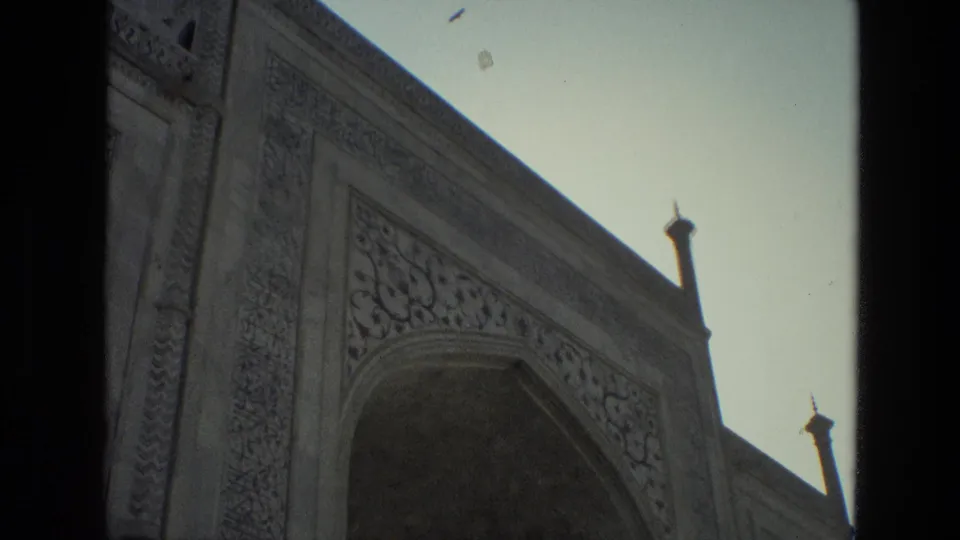 1974 India 8mm frame with a closer view of carved mosque stonework, a large arched recess, slim finials, and open sky.