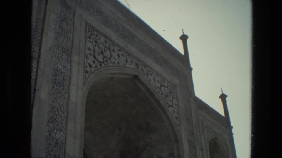 1974 India 8mm frame showing the mosque's arched entrance area, decorative stonework, roofline finials, and a bright sky.