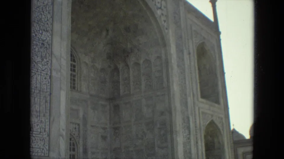 A 1974 India home-movie frame shows carved arched openings and pale monument walls, with a dark foreground strip cutting through the view.