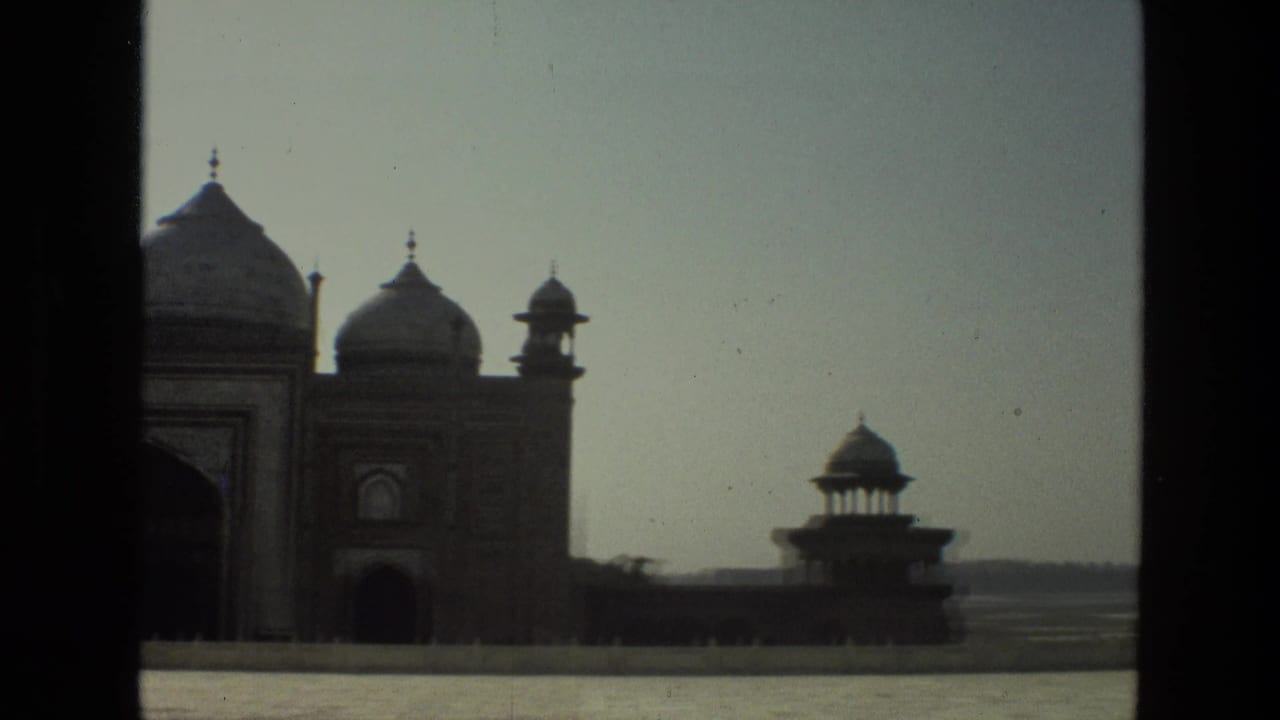 Distant Taj Mahal complex with domes and a small pavilion across an open foreground.