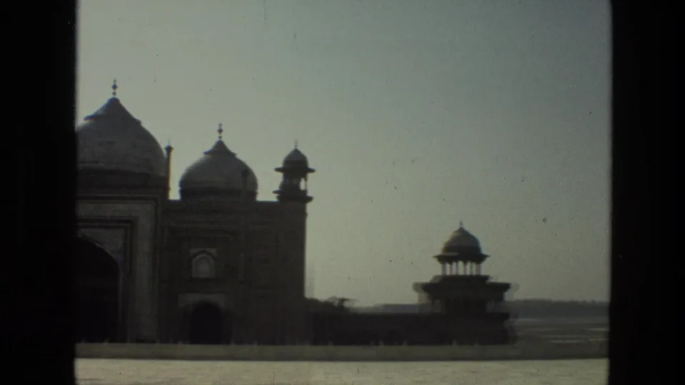 1974 India 8mm frame showing a distant view of the Taj Mahal complex, domes, side pavilion, pale sky, and dark film borders.