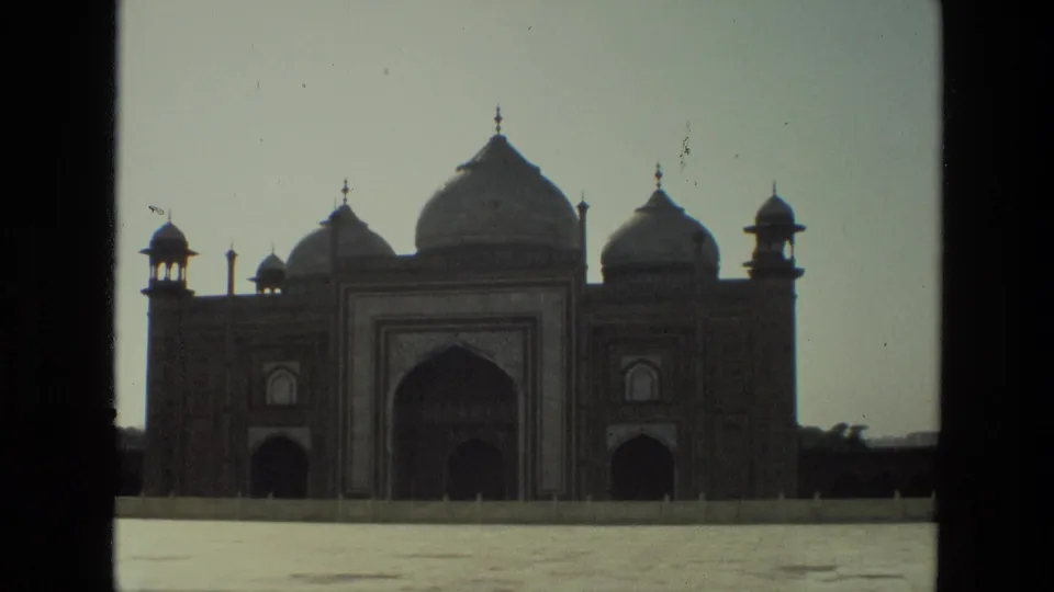 1974 India 8mm frame showing the Taj Mahal complex facade with central arch, domes, corner tower forms, and a bright open foreground.