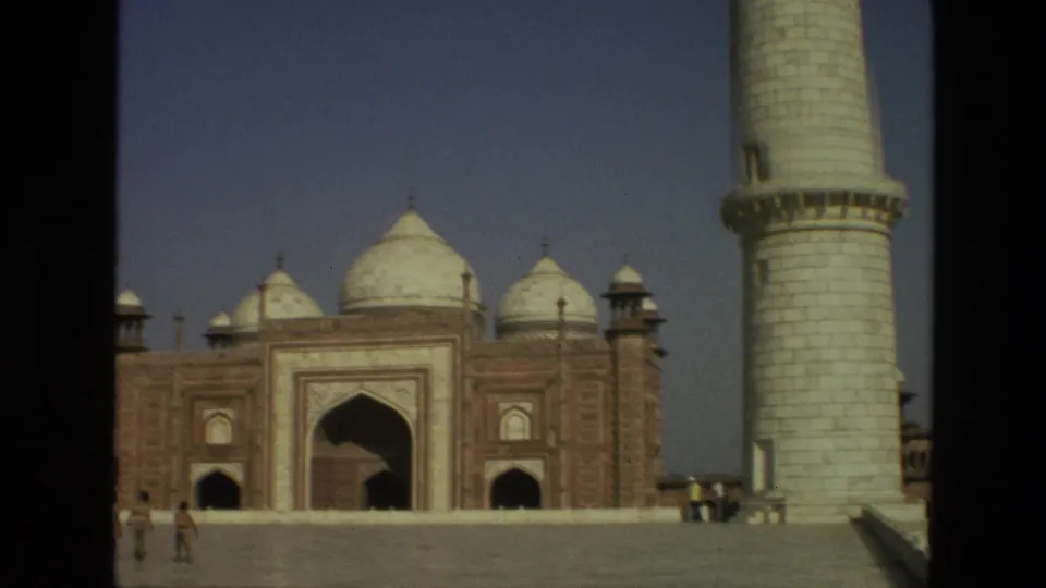 1974 8mm frame of the Taj Mahal complex with domed red sandstone gateway, minaret, marble steps, and visitors.