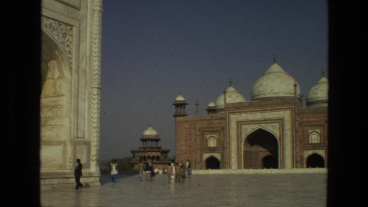 Taj Mahal courtyard with marble arch, red sandstone building, domes, and tourists walking.