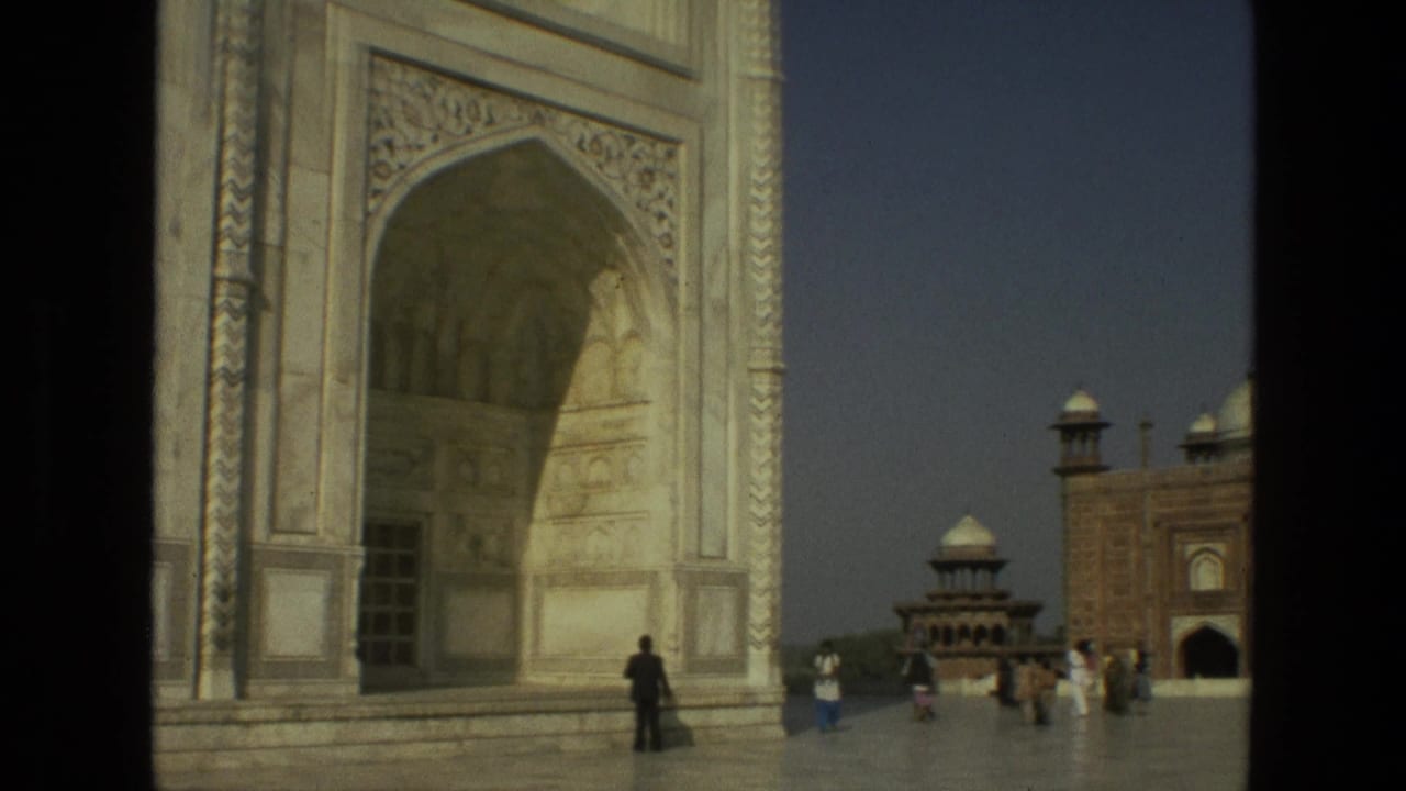 Large marble arch with calligraphy panels and tourists in the courtyard.