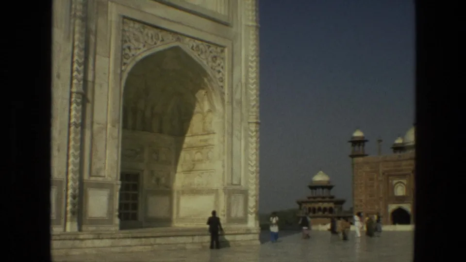 A visitor-shot 1974 frame of the Taj Mahal marble facade, showing the large arch, carved panels, and people moving across the courtyard.