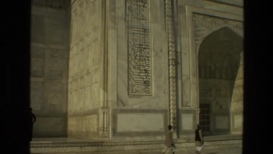 Sunlit 1974 8mm frame of Taj Mahal marble wall details, calligraphy, an arched recess, and visitors moving through the courtyard.