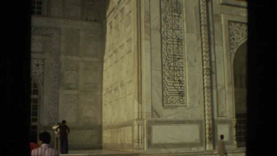 1974 India 8mm frame showing tourists at the base of a large Mughal-style stone facade with arched openings and decorative calligraphy.