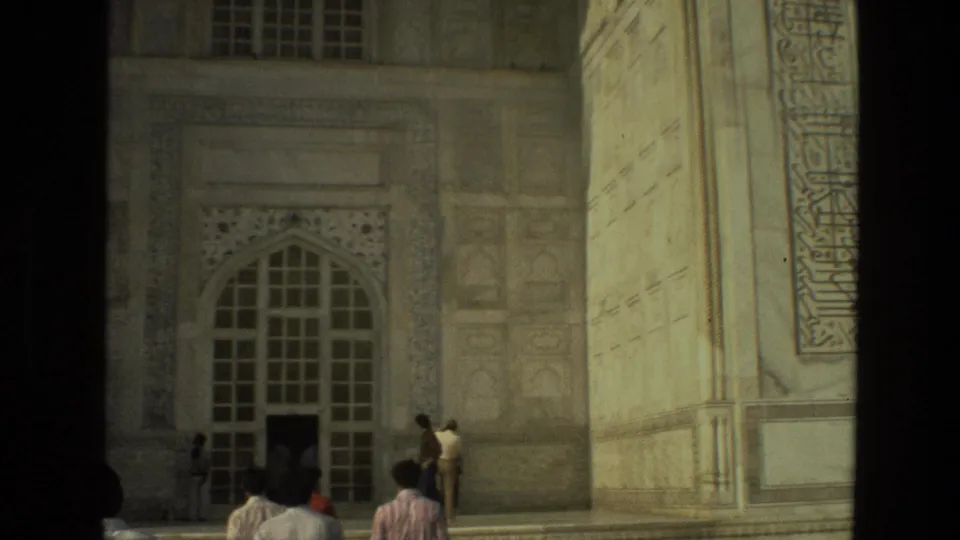 Visitors in period clothing approach a large arched doorway on a Mughal-style building in India, with ornate stonework visible around them.
