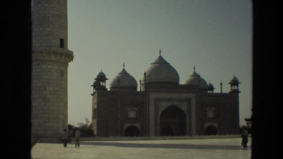 1974 8mm travel frame showing the Taj Mahal complex in India, with minaret edges, open forecourt, and a few distant visitors.