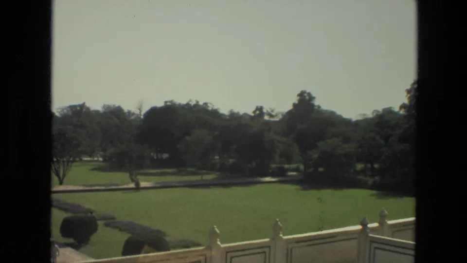 1974 India home-movie frame looking over manicured Taj Mahal garden lawns, trees, low railings, and paths under a bright sky.