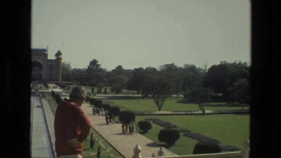 1974 India travel footage shows a visitor in a red shirt overlooking Taj Mahal garden paths with other tourists below.