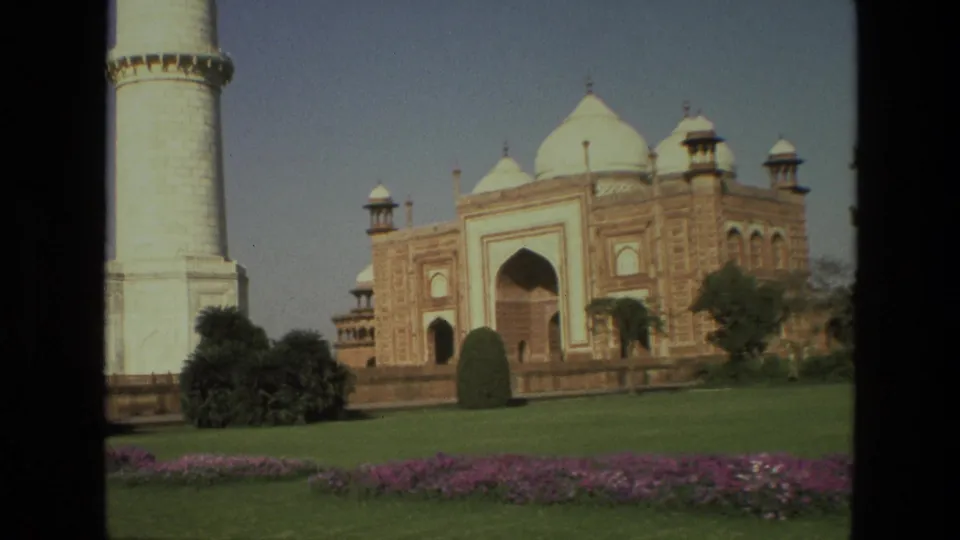 A 1974 India home-movie view shows the Taj Mahal facade, a nearby minaret, manicured lawn, shrubs, and flowerbeds.
