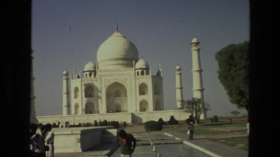 1974 India frame showing the Taj Mahal, minarets, garden paths, reflecting-pool edges, trees, and several visitors in the foreground.