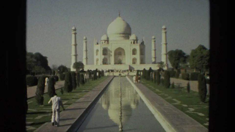 1974 home-movie frame of the Taj Mahal and its reflecting pool, with visitors walking through the garden approach.