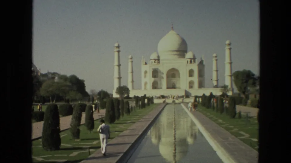 1974 home-movie view of the Taj Mahal reflected in the central pool, with manicured gardens and visitors visible in the distance.