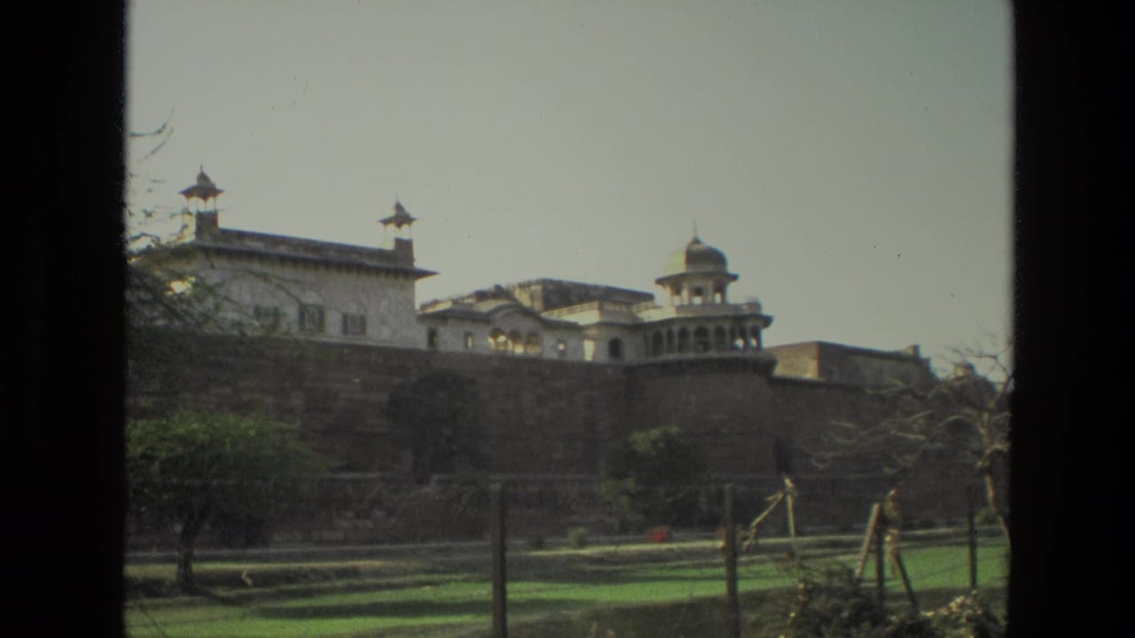 Distant palace-like building behind a wall, seen across lawns through dark film-frame borders.