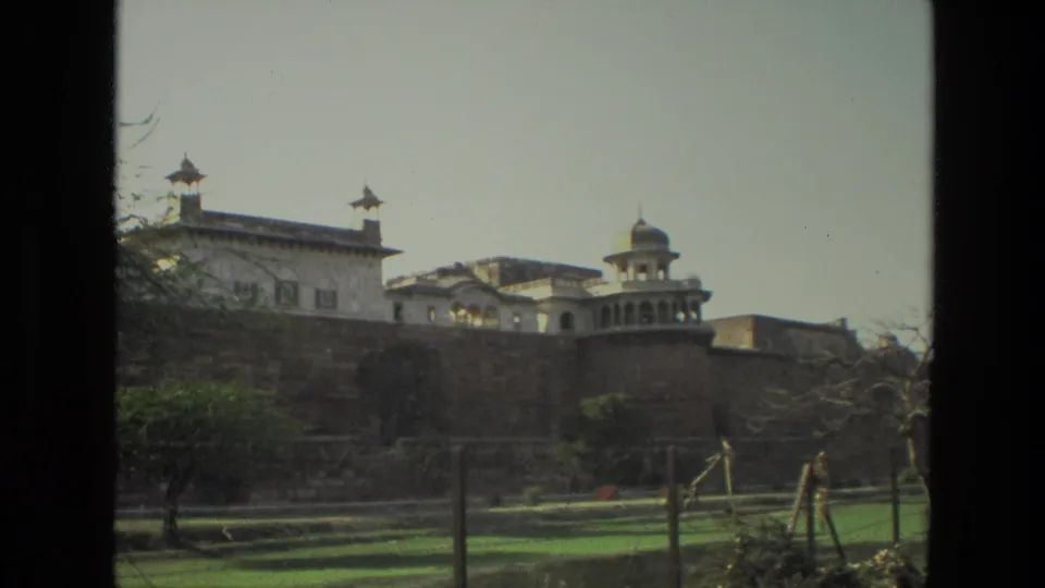1974 India 8mm frame showing a distant historic palace-like landmark, lawns, trees, and dark borders from the film scan.