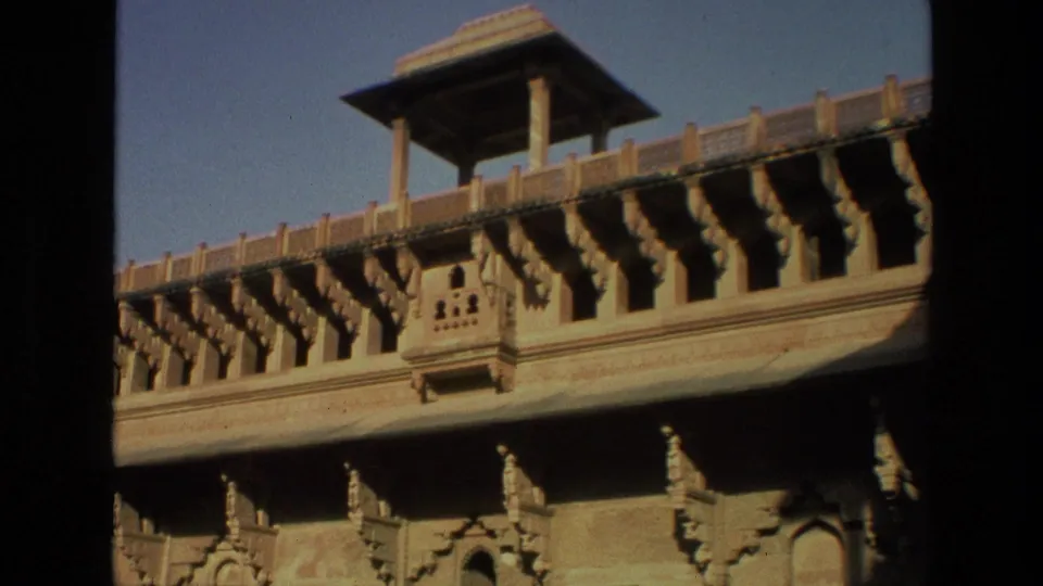 1974 India 8mm close pass by ornate palace-style stonework, showing carved supports, balcony details, and strong sunlight.