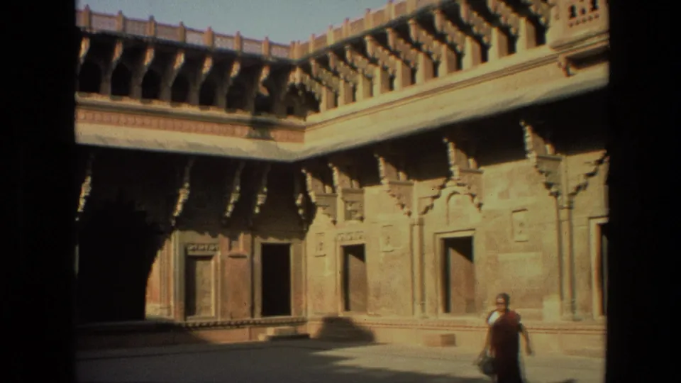 1974 India 8mm frame with a robed person near the foreground and ornate shrine courtyard architecture behind them.