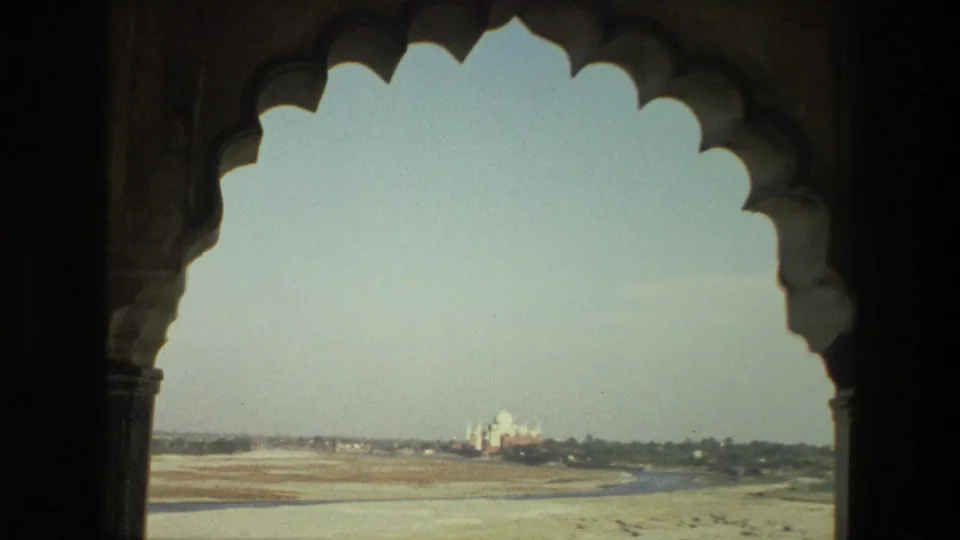 1974 India 8mm view through a dark scalloped arch, with the Taj Mahal distant across a pale riverbed and hazy sky.