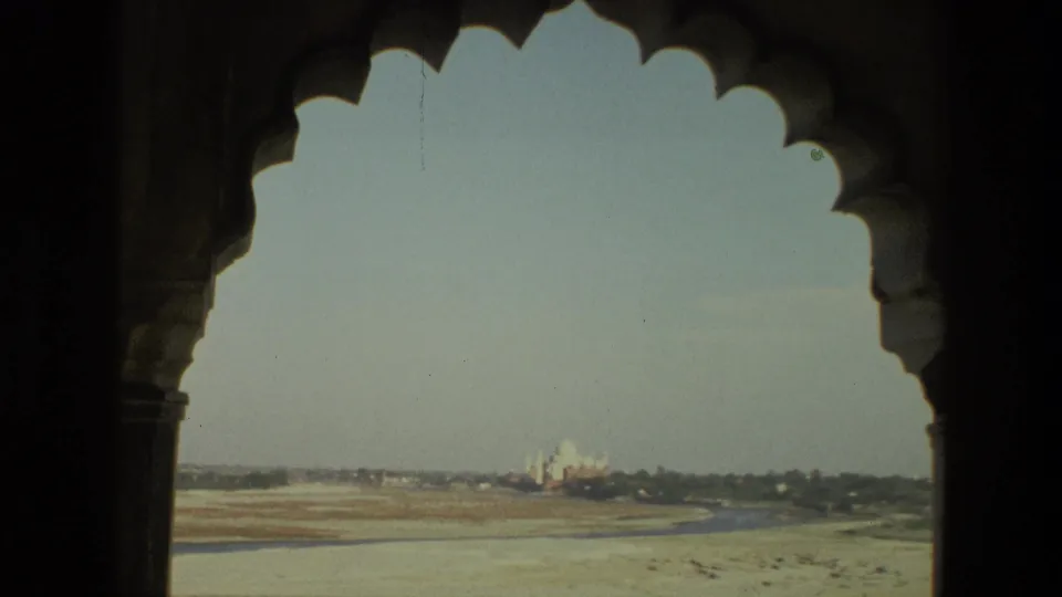1974 India 8mm frame with the Taj Mahal visible beyond a shadowed scalloped arch, dry riverbed, and low tree line.