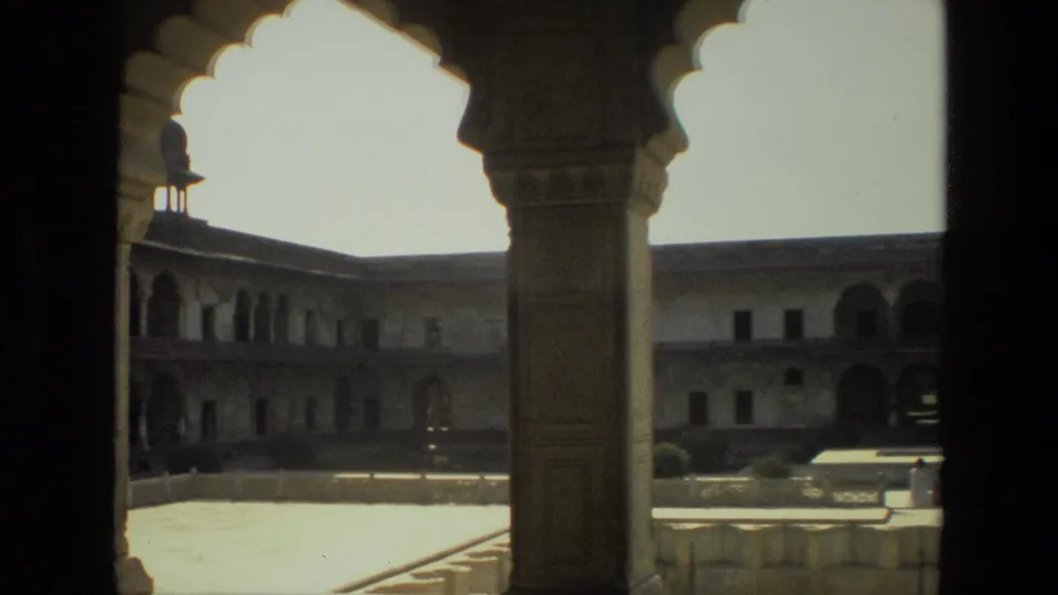 1974 India home-movie frame of courtyard architecture seen from inside a shaded arched passage, with small visitors near the building.