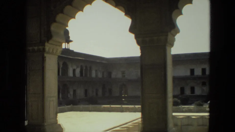 1974 India 8mm frame showing shaded stone arches opening onto a sunlit palace or fort courtyard with upper galleries.