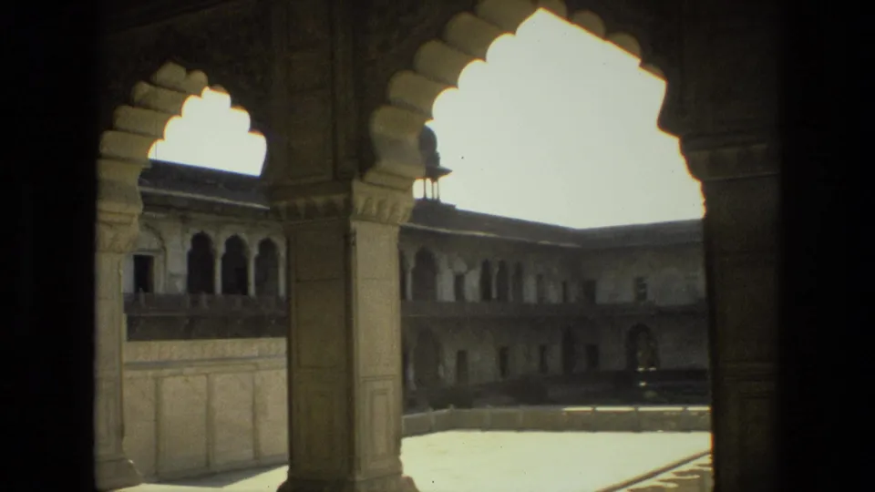 A handheld 8mm view in India frames a historic courtyard through ornate stone columns and scalloped archways.