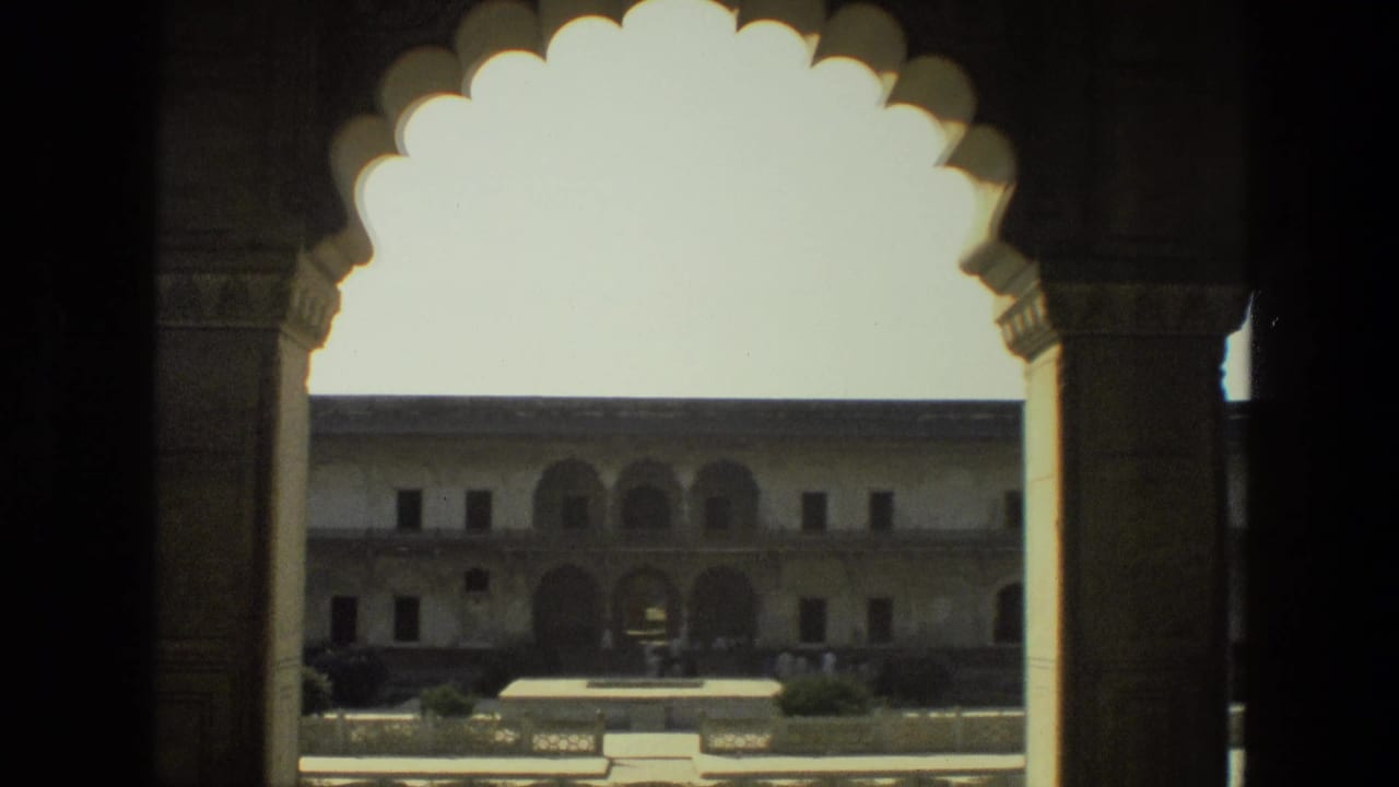 View through scalloped arches toward a sunlit courtyard and arched building.