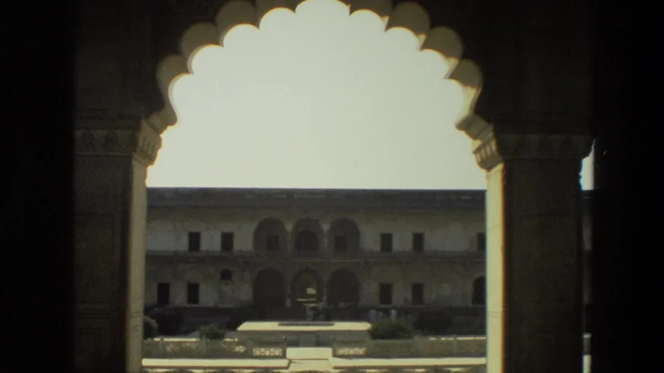 1974 India 8mm frame looking from a shaded arcade through ornate arches to a historic courtyard and arched facade.