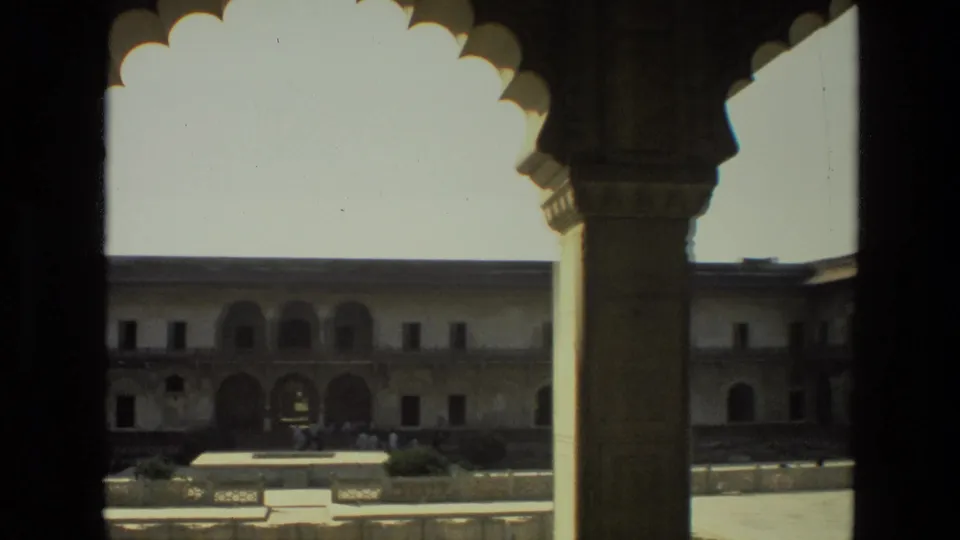 1974 India 8mm view across a bright courtyard from under a shaded arcade, with arched colonnades in the background.