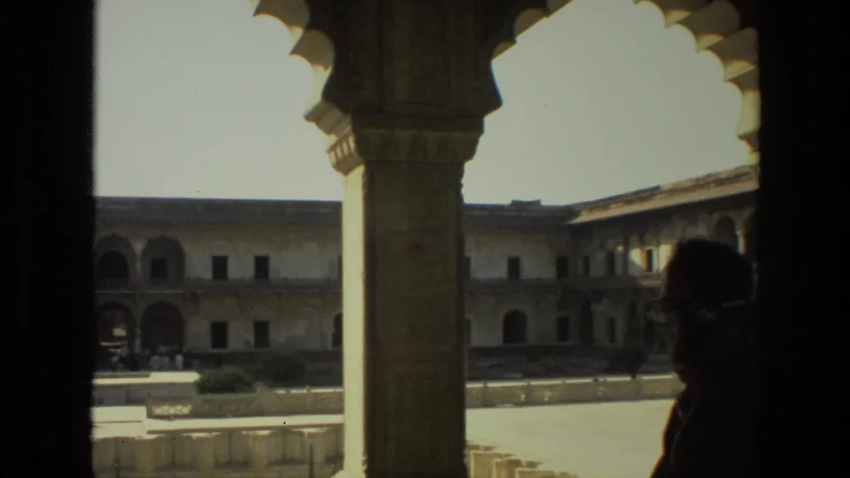 1974 India 8mm frame of a historic courtyard through columns, with a silhouetted visitor crossing the shaded foreground.