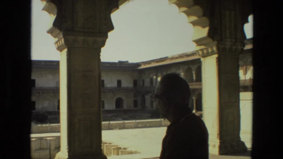 1974 India 8mm frame showing a silhouetted visitor at the edge of a shaded archway facing a sunlit historic courtyard.