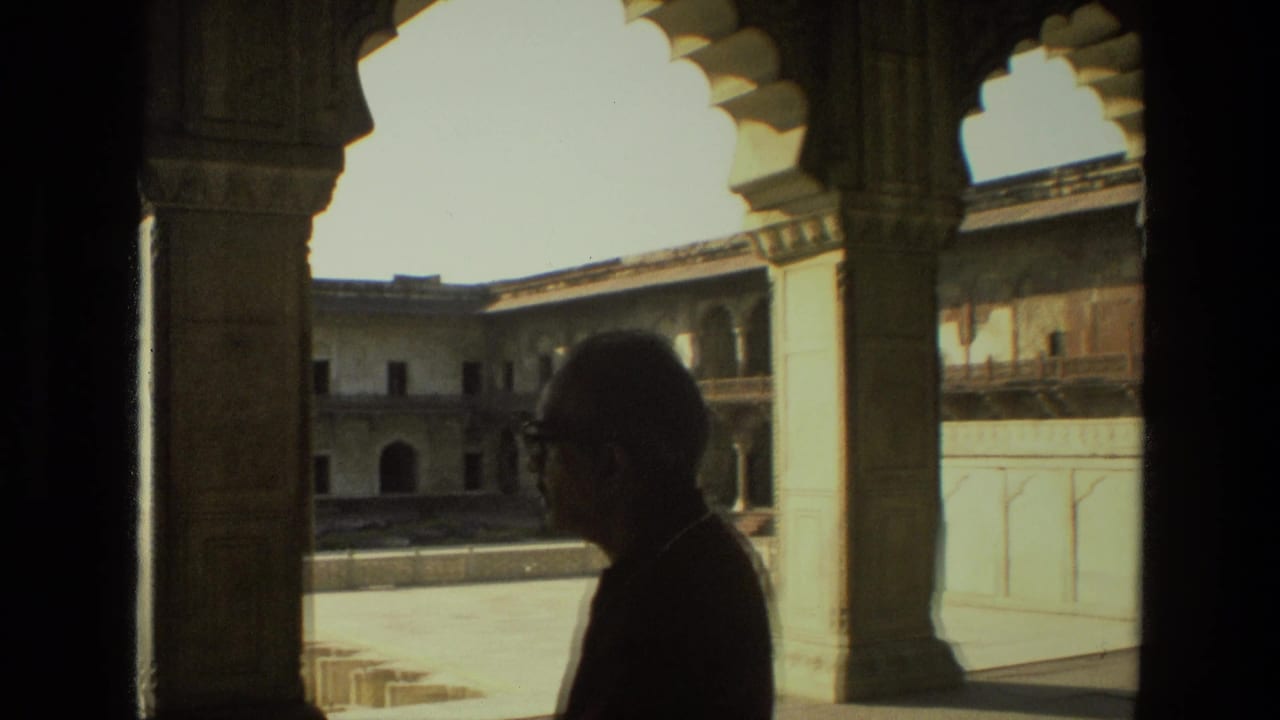 Silhouetted adult man standing under ornate arches beside a sunlit courtyard.