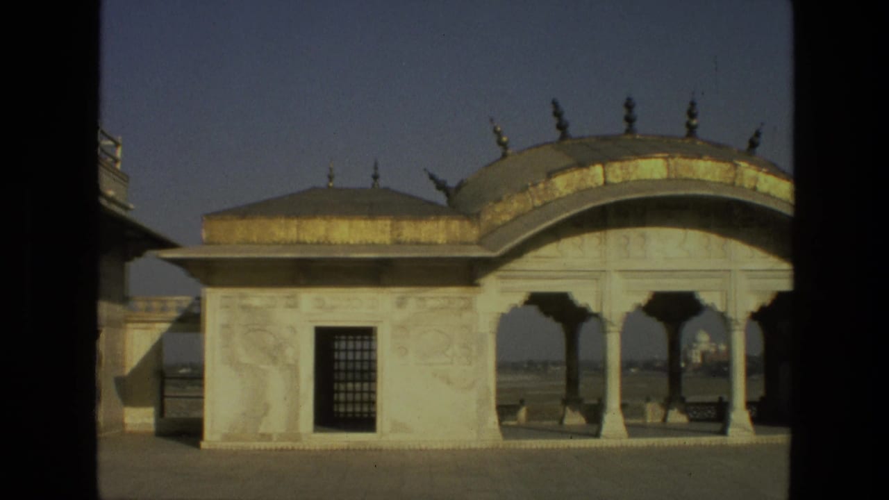 White marble pavilion with domed roof, arched openings, and a barred window under blue sky.