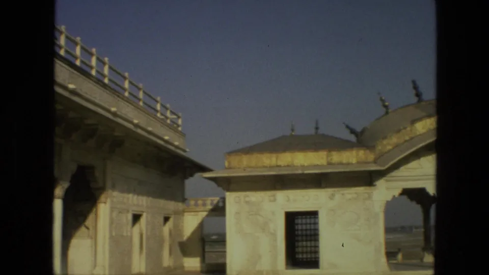 1974 India home-movie frame with a raised carved walkway, marble pavilion facade, domed roofline, and open sky.
