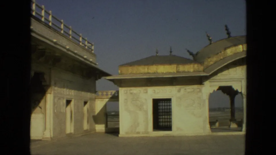 1974 India 8mm frame showing a white carved pavilion, arched opening, domed roof, and courtyard from a shaded vantage.
