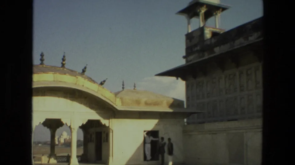 1974 India frame with pavilion arches, distant Taj Mahal, small visitors, and a tall watchtower-like structure along the right edge.