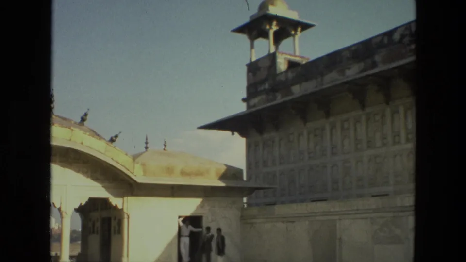 1974 India home-movie frame showing pale palace architecture, a curved roofline, and visitors in a shaded courtyard view.